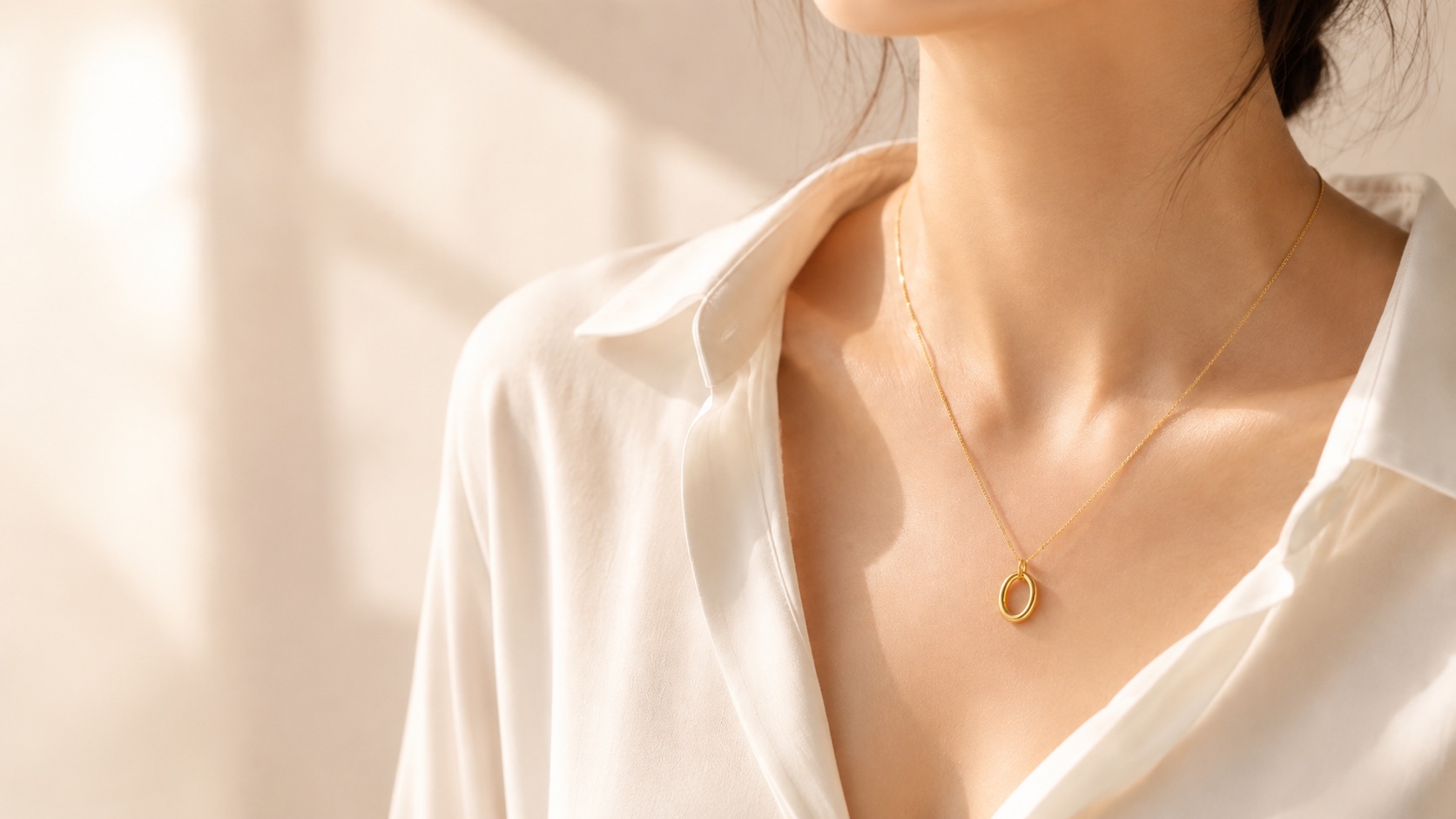 The Hollow Oval necklace close to the collarbone with white fabric.